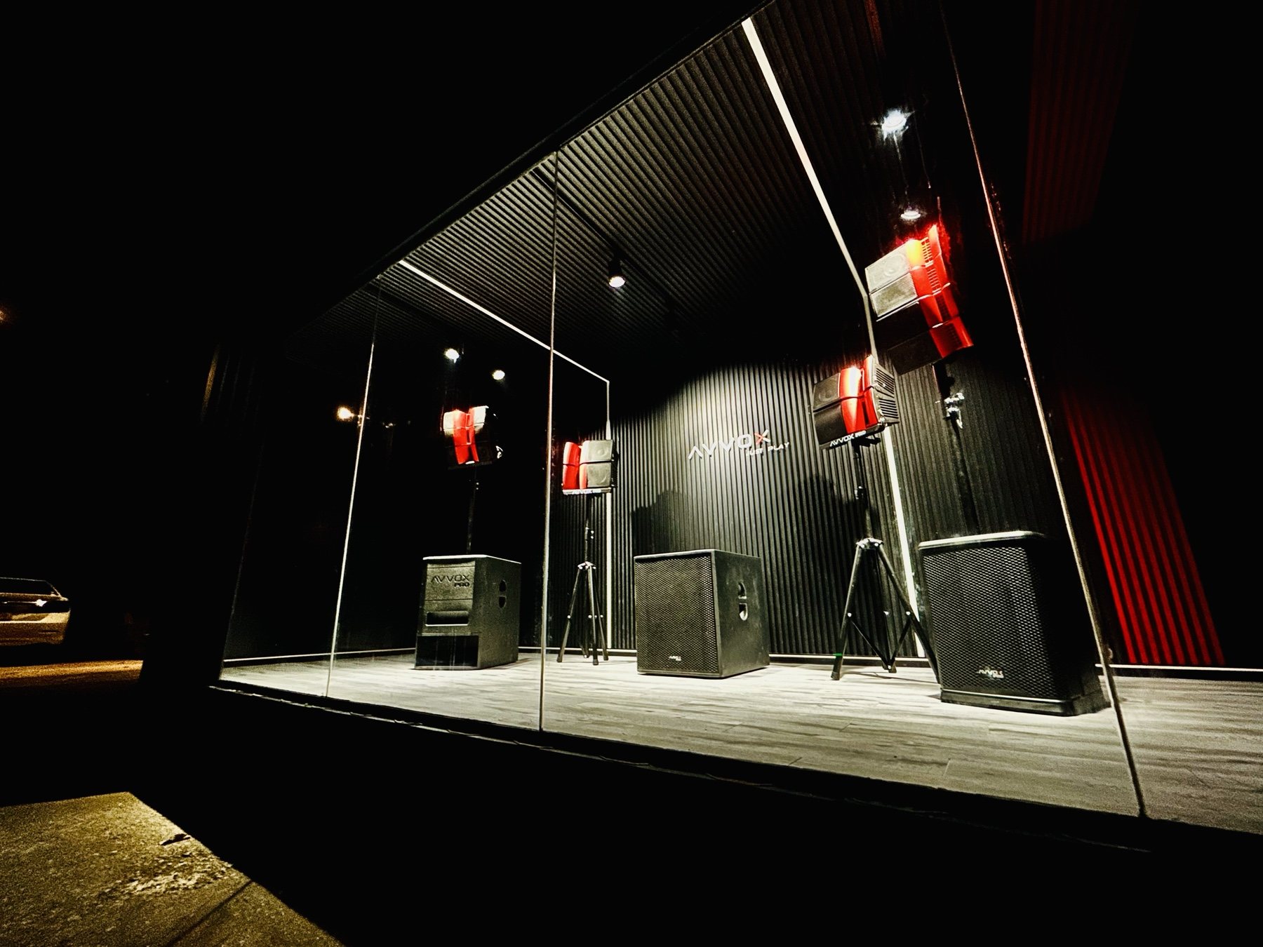 Inside the AVVOX showroom: dark ribbed walls, speakers on stands, strip lighting