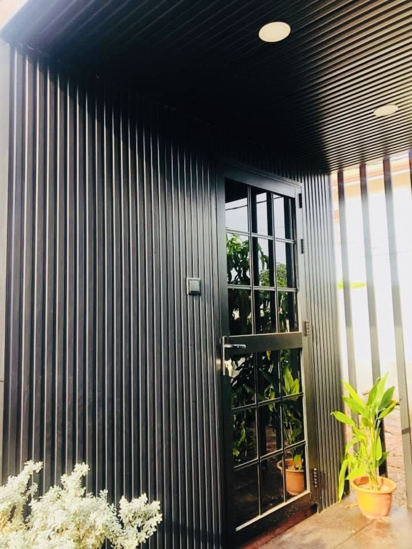 Black ribbed container entrance with a glass door and plants