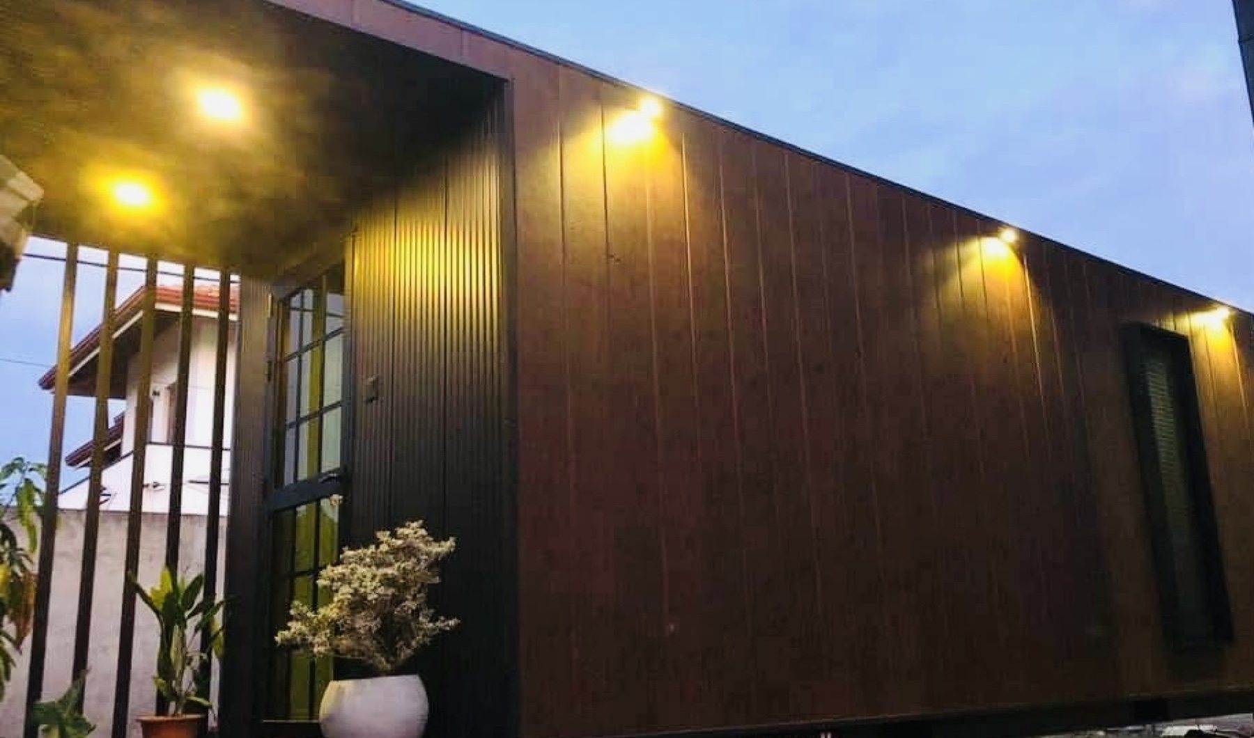 Timber-clad container office unit with warm exterior lights at dusk
